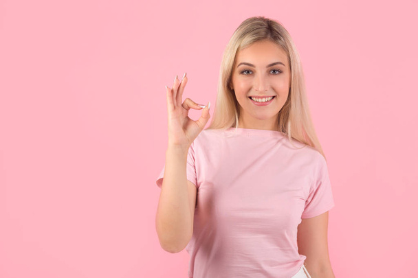 beautiful young woman on pink background with hand gesture - Foto, Imagen