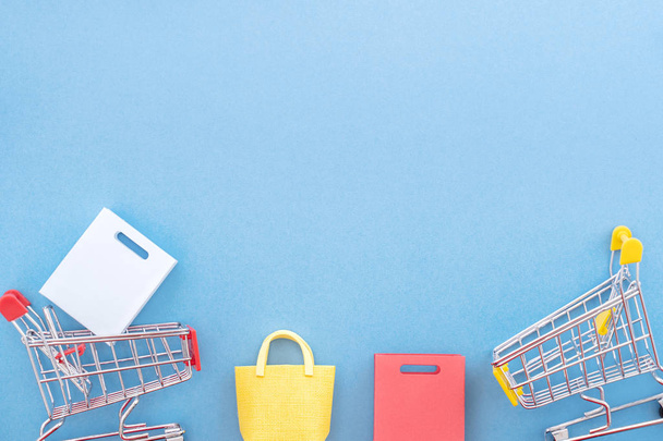 Abstract design element, concept of annual sale, shopping season - mini yellow cart with paper bag isolated on pastel blue background, top view, flat lay. - 写真・画像