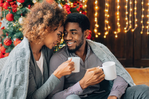クリスマスツリーでコーヒーを飲む若いカップル - 写真・画像