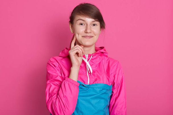 Portrait of smiling young woman looking directly at camera, standing isolated over pink background, attractive female wearing sporty blue rose shirt, keep sher index finger on cheek. People concept. - Fotó, kép