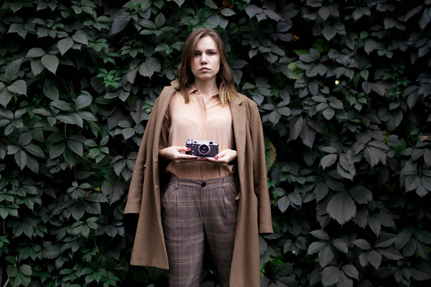 joven fotógrafa se para con una cámara de cine cerca de una pared de hojas en el bosque, una mujer fotografía en la naturaleza
 - Foto, imagen