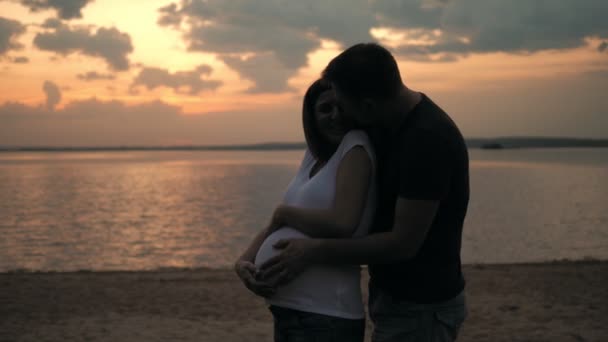 Marito abbraccia la sua amata moglie incinta in piedi sulla spiaggia al tramonto
 - Filmati, video