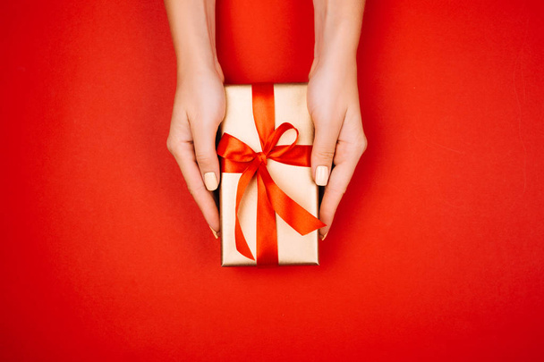 Beautiful young female hands holding a golden gift with a red bow. Christmas concept. - Zdjęcie, obraz