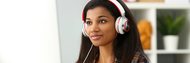 Black smiling woman sitting at workplace wearing headphones - Valokuva, kuva