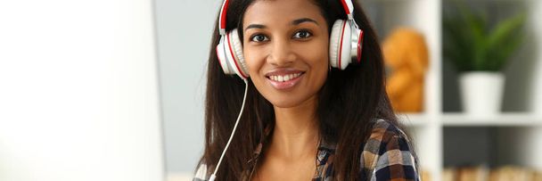 schwarz lächelnde Frau sitzt mit Kopfhörern am Arbeitsplatz - Foto, Bild