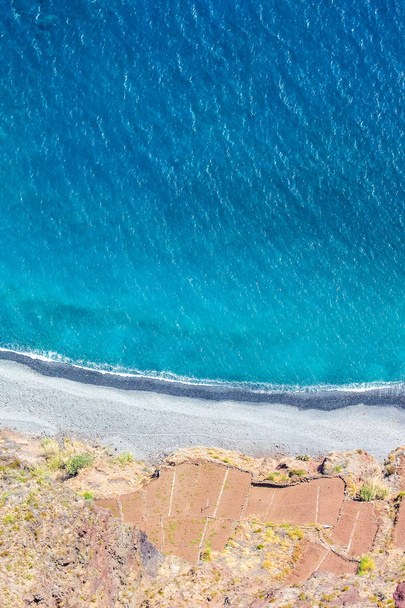 Aerial landscape by the blue Atlantic ocean. Stone beach and adjacent fields on the southern coast of Madeira Island, Portugal. Aerial view, amazing nature. Summer vibes on a vertical photo - Photo, Image