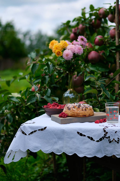 村のリンゴの木の下の古い木製のテーブルの上にアップルパイ。明るい晴れた日とコンポートとおいしい自家製デザート. - 写真・画像
