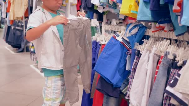 little customer boy selects new clothes in fashion store during seasonal discounts - Footage, Video