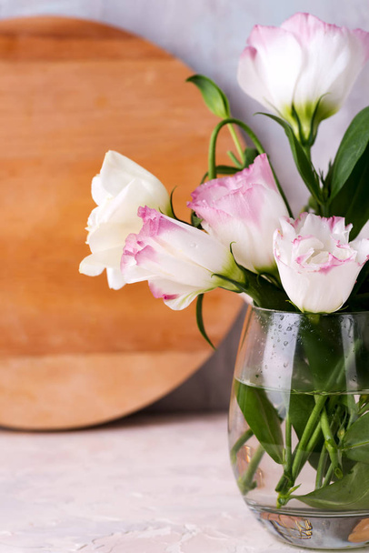 Eustoma flowers in vase on table near wooden plate and stone wall, close-up. Blank for postcards - Photo, Image