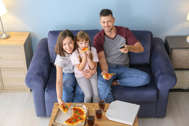 Happy family eating pizza while watching TV at home - Fotó, kép