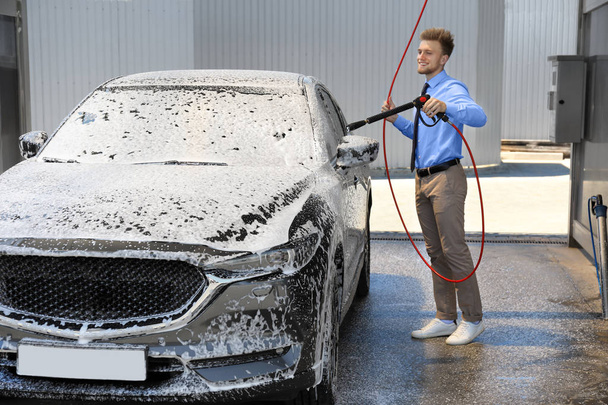 Businessman cleaning auto with high pressure water jet at self-service car wash - Фото, зображення