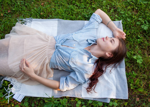 a woman in a bright shirt lying on the grass in a public Park and enjoys his life of solitudel - Foto, Imagem