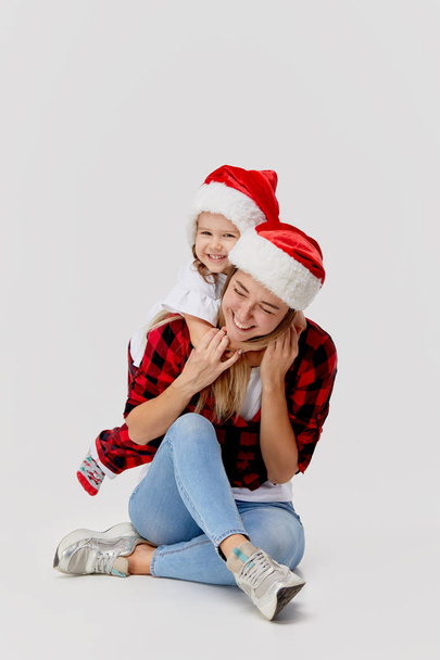Christmas time. Happy hugging family, mother and daughter, little child playing in Santa hats, isolated on white. New year holiday concept - Foto, afbeelding