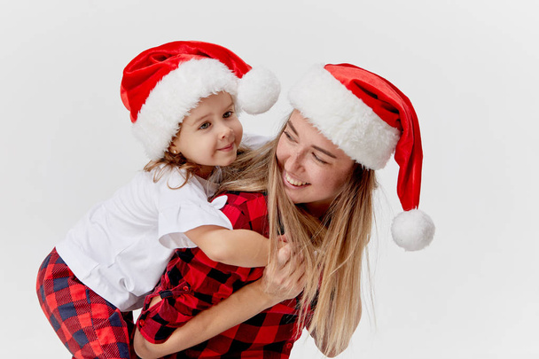 Christmas time. Happy hugging family, mother and daughter, little child playing in Santa hats, isolated on white. New year holiday concept - Foto, Imagen