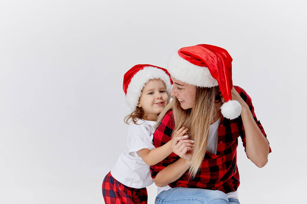 Christmas time. Happy hugging family, mother and daughter, little child playing in Santa hats, isolated on white. New year holiday concept - Foto, imagen