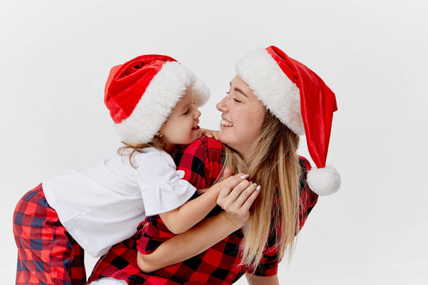 Christmas time. Happy hugging family, mother and daughter, little child playing in Santa hats, isolated on white. New year holiday concept - Fotografie, Obrázek