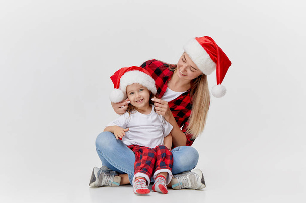 Christmas time. Happy hugging family, mother and daughter, little child playing in Santa hats, isolated on white. New year holiday concept - Foto, immagini