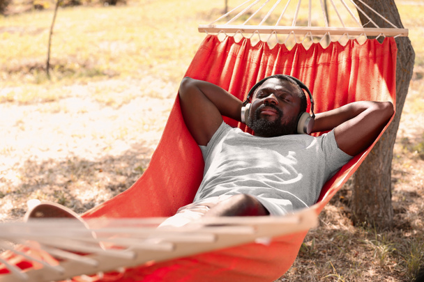 Hombre afroamericano escuchando música mientras se relaja en la hamaca al aire libre
 - Foto, Imagen