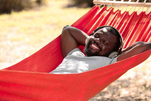 Афроамериканец слушает музыку во время отдыха в гамаке на открытом воздухе
 - Фото, изображение