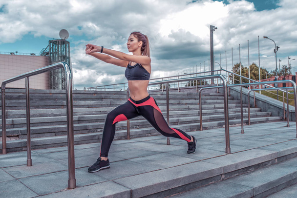 Beautiful girl athlete doing stretching muscles in the summer in the city before jogging, sportswear, top leggings, sneakers, active fitness lifestyle, outdoor sports exercise. - Fotó, kép