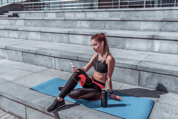 Beautiful girl athlete, resting after hard workout, summer autumn and spring in city, smartphone headphones enjoys music relaxes, free space motivation text, active fitness lifestyle, outdoor sports. - Foto, Imagem