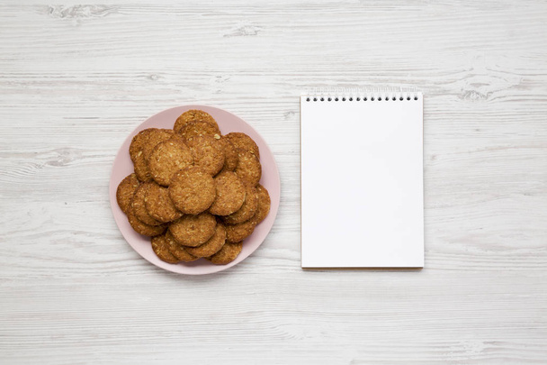 Cereal cookies on a pink plate, blank notepad on a white wooden  - Photo, Image