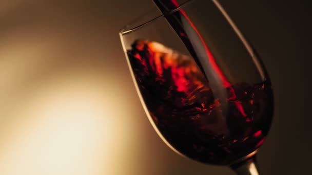 Slow motion of pouring red wine from bottle into goblet with copy space at left. Close-up of red wine forms beautiful wave in glass. Wine pouring in glass at dark background. - Séquence, vidéo