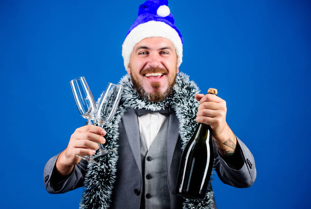 Vállalati karácsonyi buli. Kreatív tószt. Egészségedre! Csatlakozz az irodai bulihoz. A szakállas hipszter télapósapkát visel, pezsgős üveget tart. Ünnepeljük az új évet. Karácsonyi buli. Vállalati parti ötletek - Fotó, kép