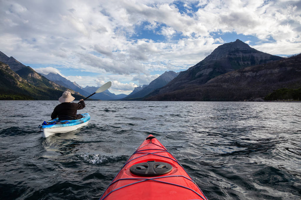 Adventurous Man Kayaking in Glacier Lake surrounded by the beautiful Canadian Rocky Mountains during a cloudy summer sunset. Taken in Upper Waterton Lake, Alberta, Canada. - Фото, зображення