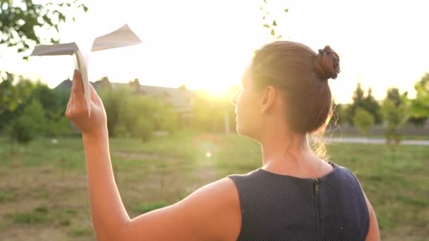 女性は日没の背景に紙飛行機を起動します。旅行やスチュワーデスの職業の夢。スローモーション - 映像、動画