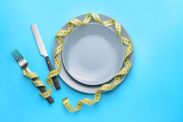 Cutlery with plates and measuring tape on color background. Concept of diet - 写真・画像