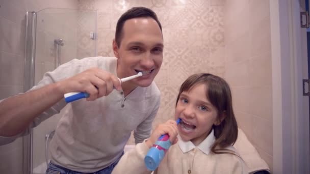 mondhygiëne, vrolijke vader met dochter met tandenborstel tanden poetsen voor spiegel - Video