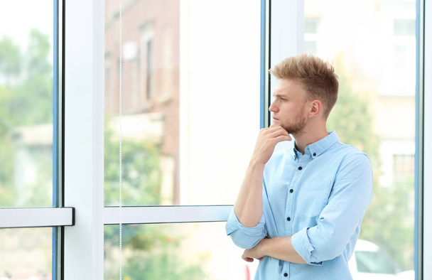 Portrait of handsome young man looking out window indoors - Foto, Imagen