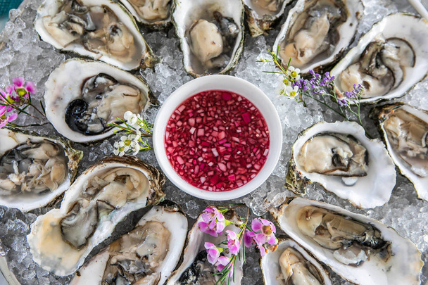 Top View Of Fresh Opened Oysters On Ice, Decorated With Herbs And Flowers, And Vinegar. Selective Focus On Mollusc. - Foto, Imagem