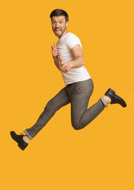 Mies hyppää osoittaa sormella kameraa, keltainen tausta
 - Valokuva, kuva