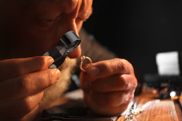 Male jeweler evaluating diamond ring in workshop, closeup view - Photo, Image