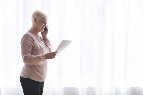 Vanhempi nainen, jolla on paperit ja puhuu puhelimessa asiakkaiden kanssa
 - Valokuva, kuva