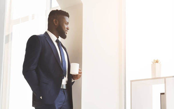Handsome african businessman drinking coffee near window in office - Photo, Image