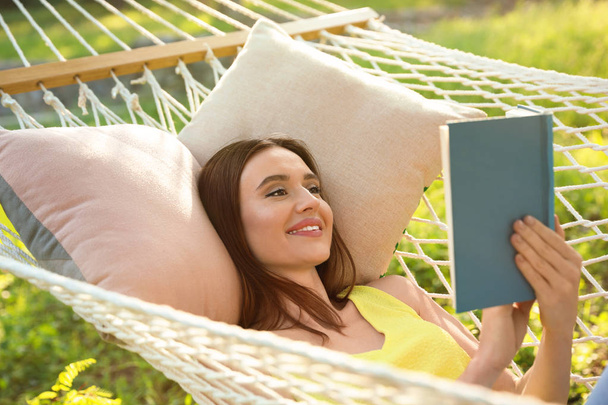 Jeune femme lisant le livre dans l'hamac confortable au jardin vert - Photo, image