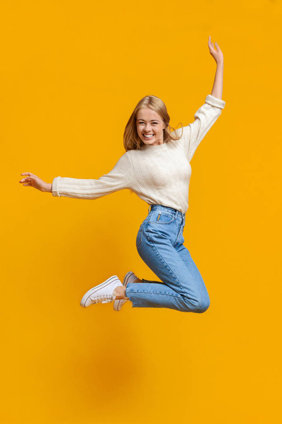 Teenage girl having fun jumping in air on orange background - 写真・画像