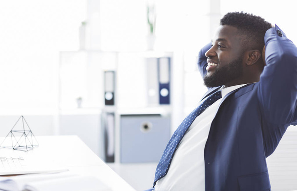 Dreamy african businessman leaning back in modern office - Foto, immagini