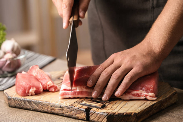 Man cutting fresh raw meat on table in kitchen, closeup - 写真・画像