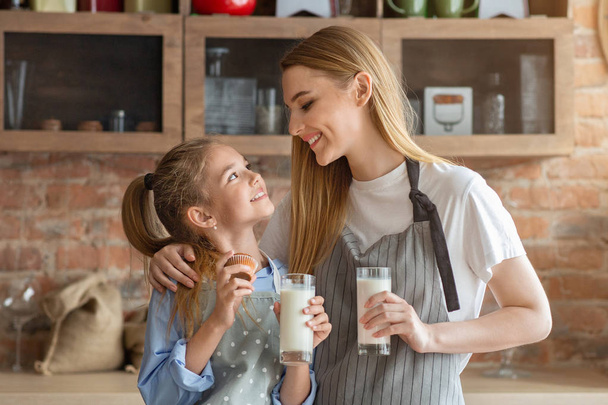 Pretty mom and daughter drinking milk at kitchen - Photo, image