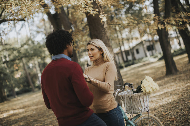 Многорасовая молодая пара с велосипедом, стоящая в осеннем парке
 - Фото, изображение