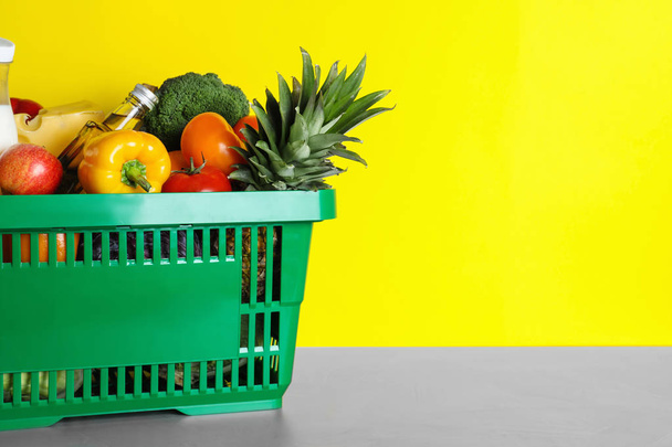 Shopping basket with grocery products on grey table against yellow background. Space for text - Фото, изображение