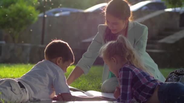 educação pré-escolar, belo livro de leitura feminina para menino e menina sentados na grama verde ao ar livre em luz ensolarada
 - Filmagem, Vídeo