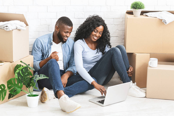 Couple joyeux assis sur le sol dans un nouvel appartement, à l'aide d'un ordinateur portable
 - Photo, image