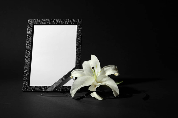 Funeral photo frame with ribbon and white lily on black background. Space for design - Foto, afbeelding