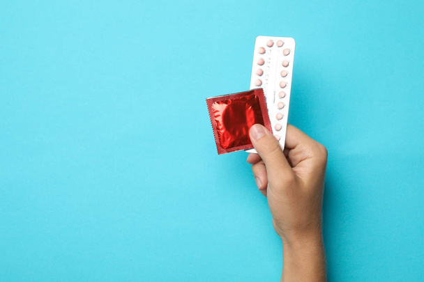 Woman holding condom and birth control pills on blue background, top view with space for text. Safe sex - Φωτογραφία, εικόνα