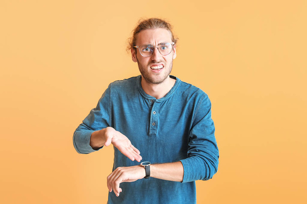 Gestresster junger Mann mit Uhr auf farbigem Hintergrund - Foto, Bild